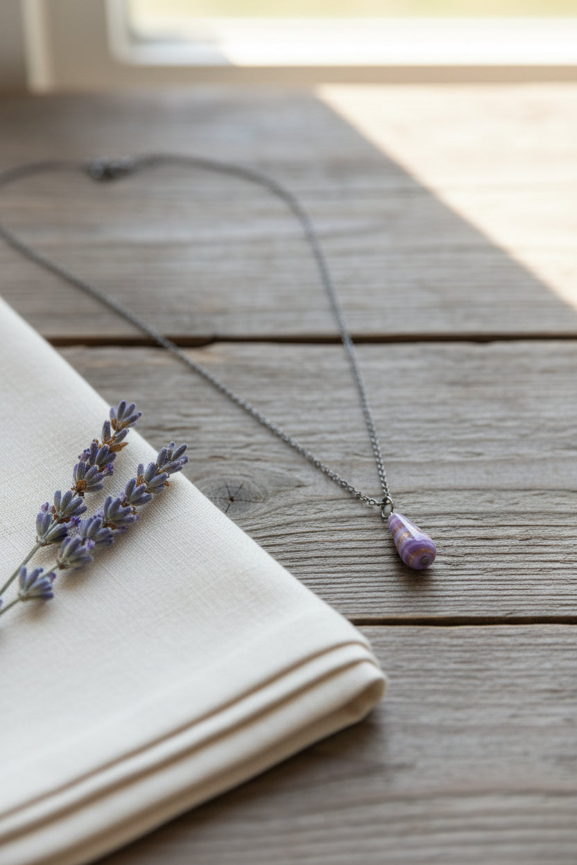 A silver chain necklace with a teardrop-shaped pendant featuring purple and white horizontal stripes, displayed on a black velvet jewelry bust.