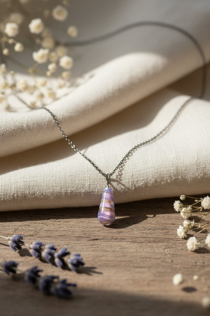 A silver chain necklace with a small teardrop-shaped pendant featuring lavender purple and orange horizontal stripes, displayed on a black velvet jewelry bust.