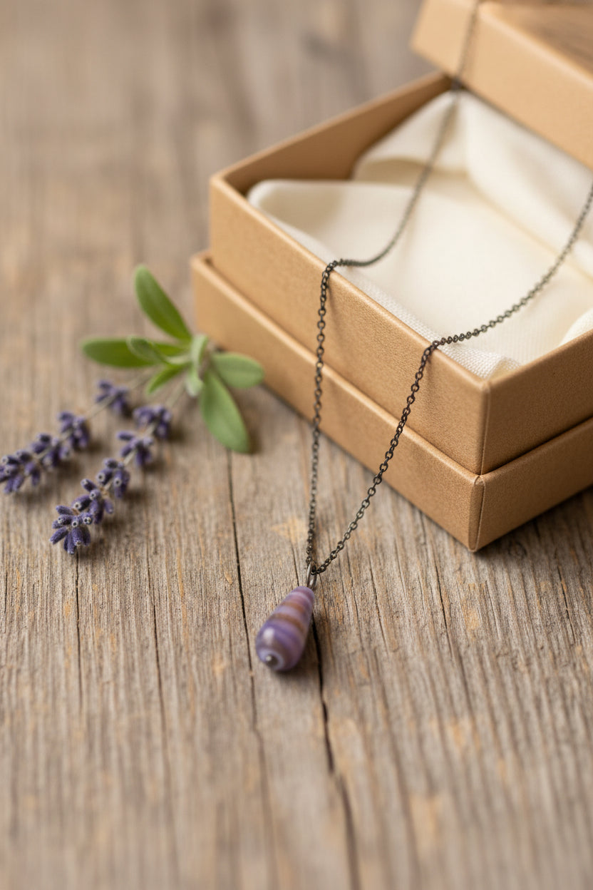 A silver chain necklace with a teardrop-shaped pendant featuring horizontal lavender, purple, and orange stripes, displayed on a black velvet jewelry bust against a white background.