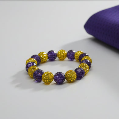 A beaded stretch bracelet featuring alternating purple and gold textured round beads, displayed on a plain light gray background.