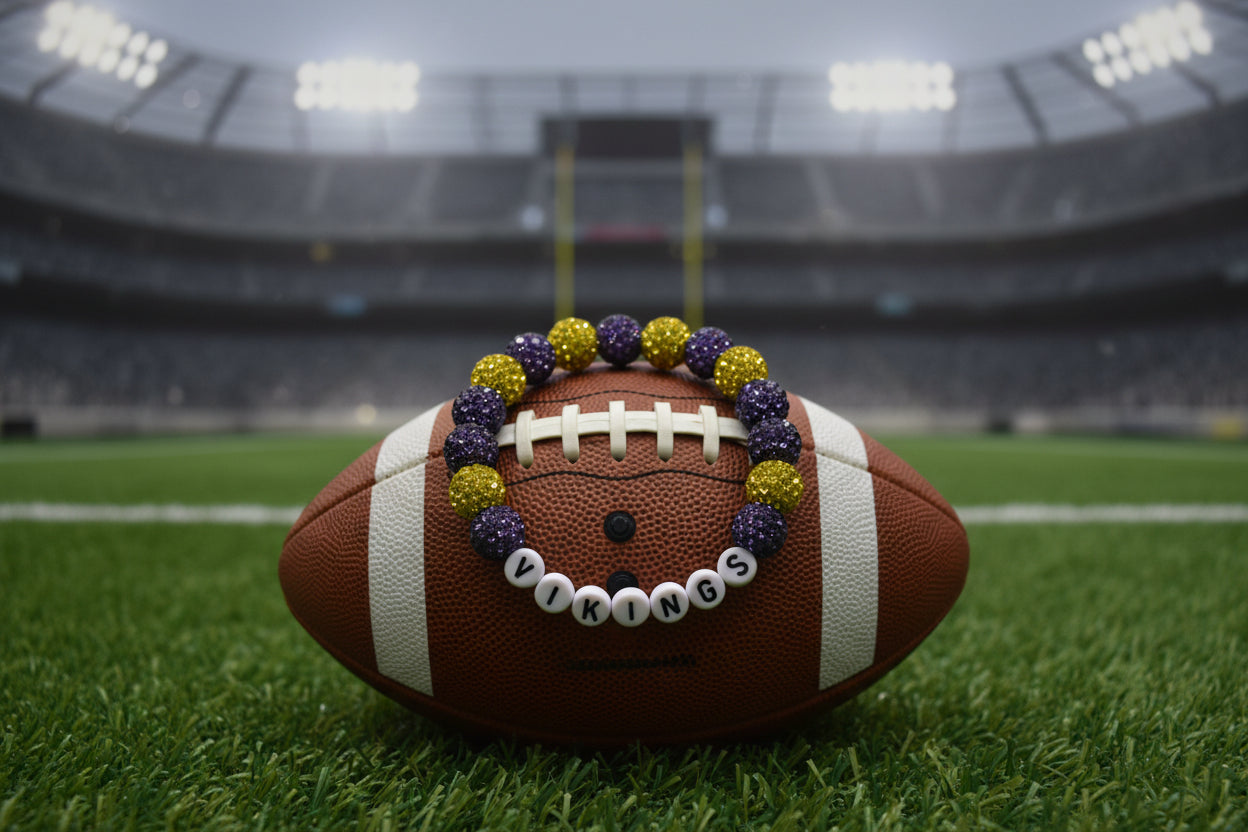 A beaded stretch bracelet featuring purple and gold glittery round beads alternating with white letter beads that spell 'VIKINGS' on a plain light gray background.