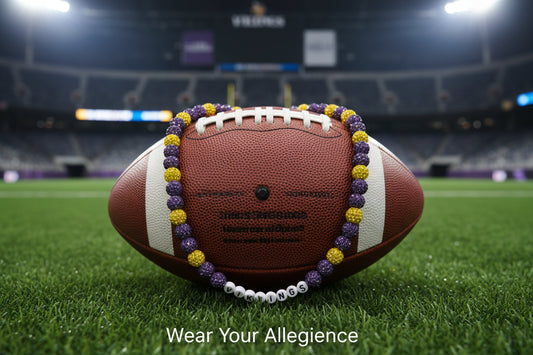 A beaded necklace with purple and gold beads, featuring white letter beads spelling 'VIKINGS' in the center, displayed on a white background.