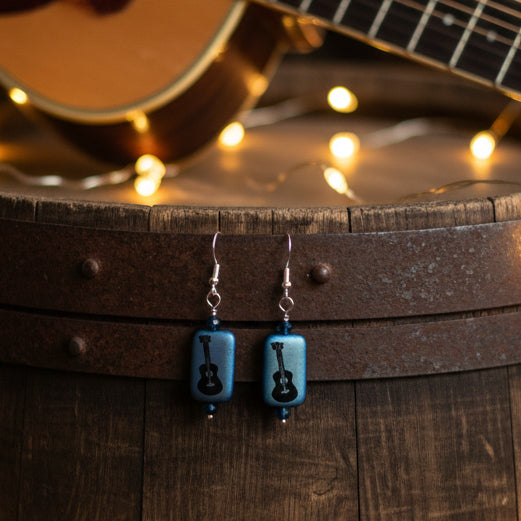 Pair of earrings with blue rectangular beads and black guitar-shaped beads on a gray background