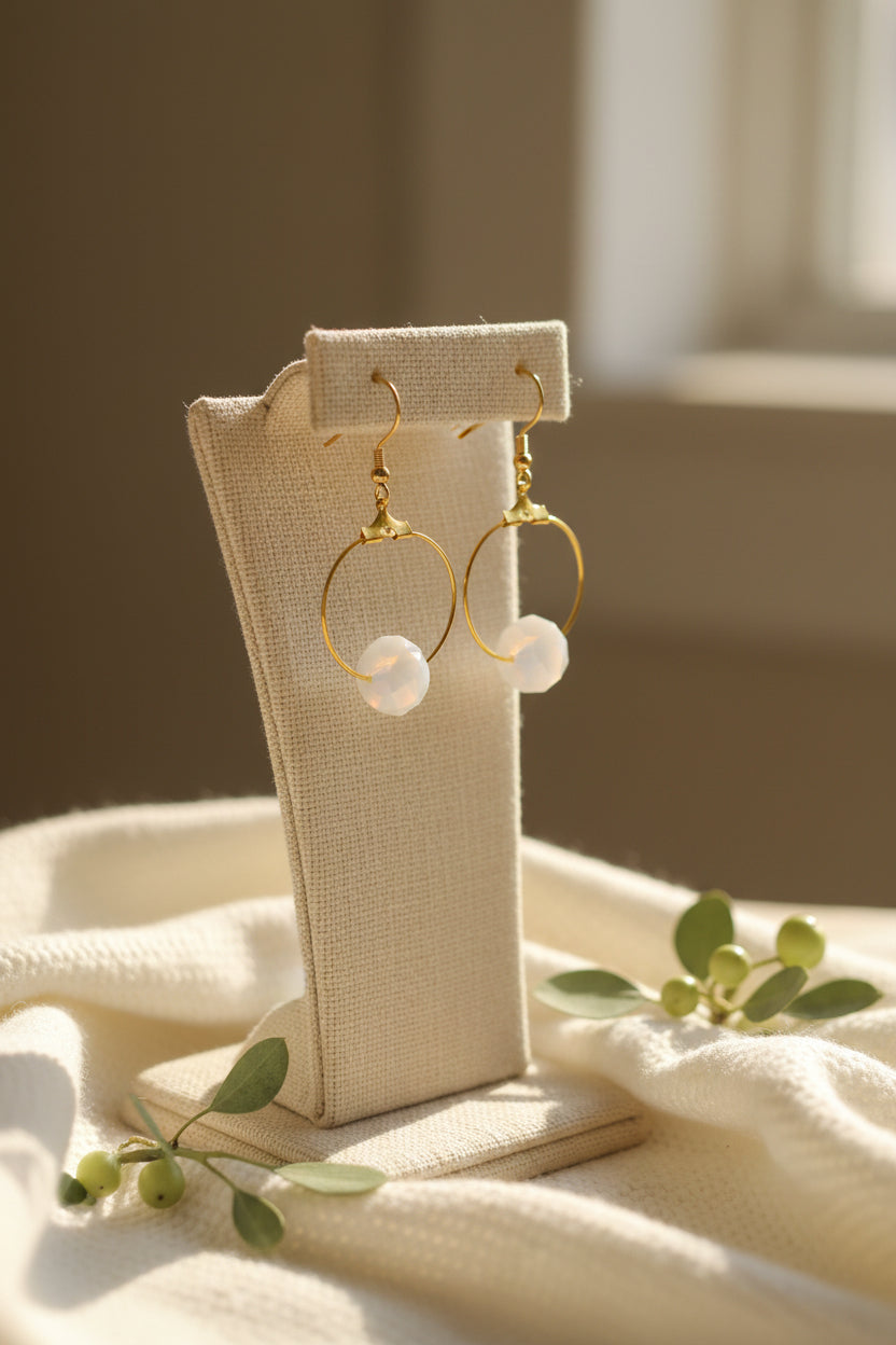 A pair of gold hoop earrings with white pearl-like drops, hanging from gold fishhook wires against a light gray background.