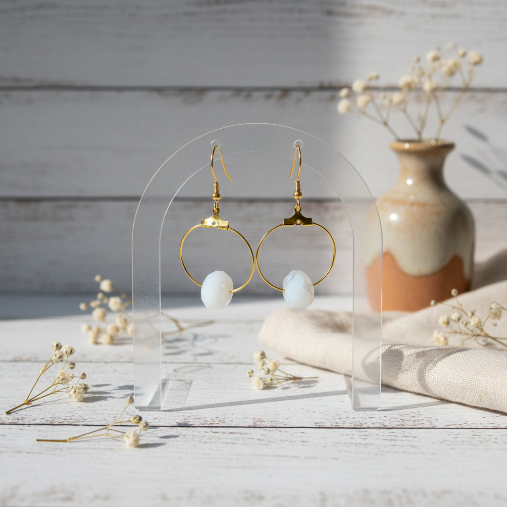 A pair of gold hoop earrings with white shell-like beads hanging from gold fishhook wires, displayed against a light gray background.