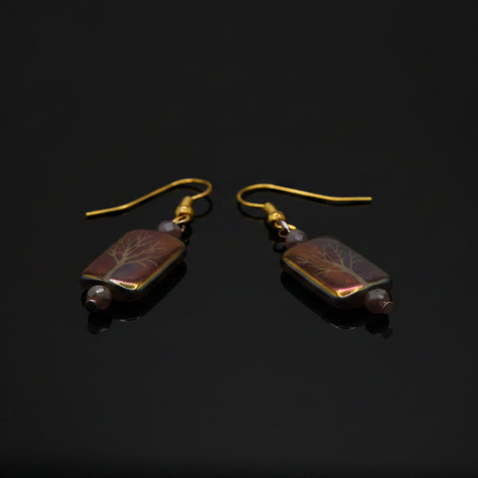 Pair of earrings with rectangular beads on a clear stand against a gray background