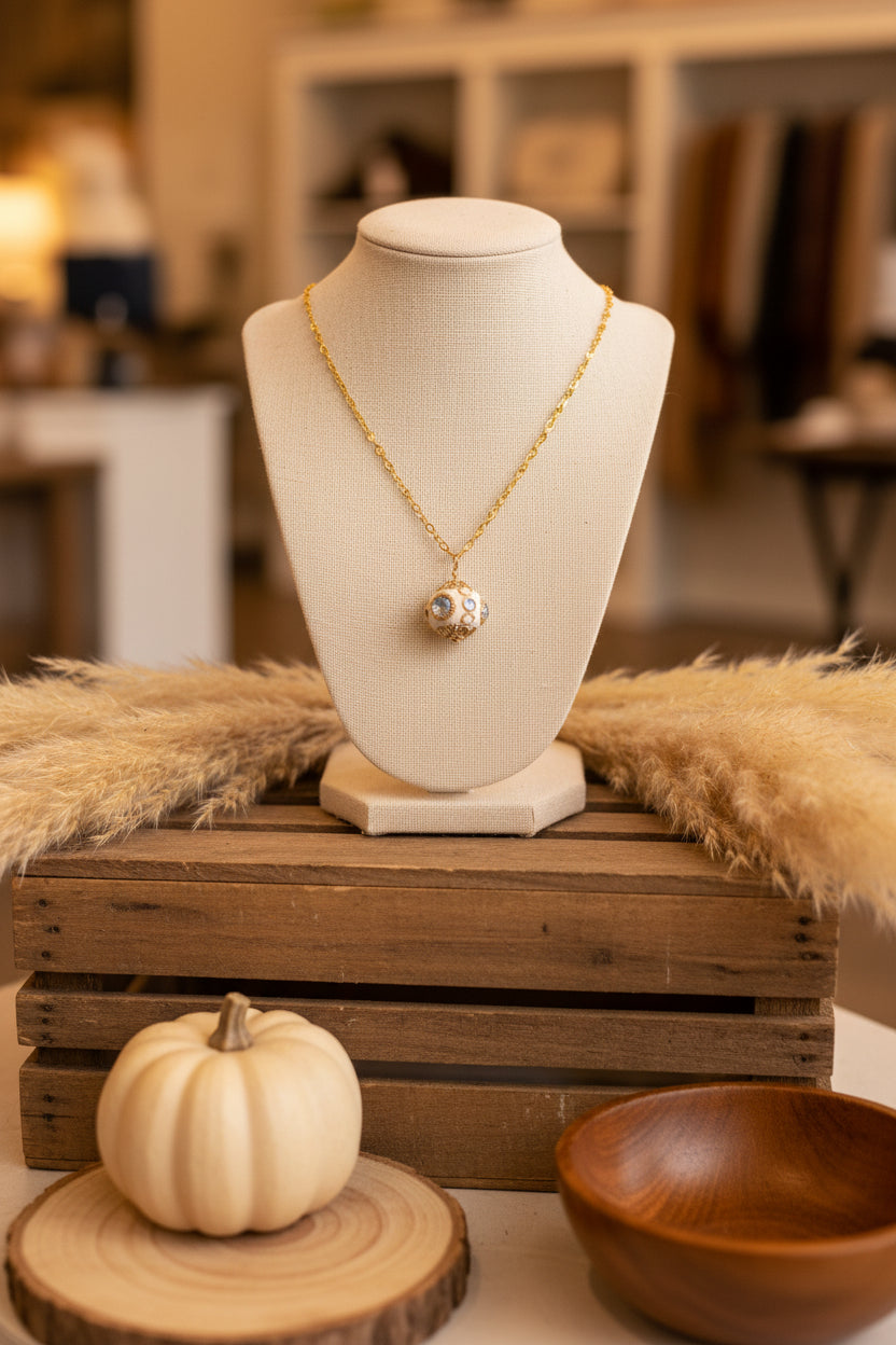 A gold chain necklace with a small round pendant featuring a central blue stone and surrounding rose gold filigree, displayed on a black velvet jewelry bust against a white background.